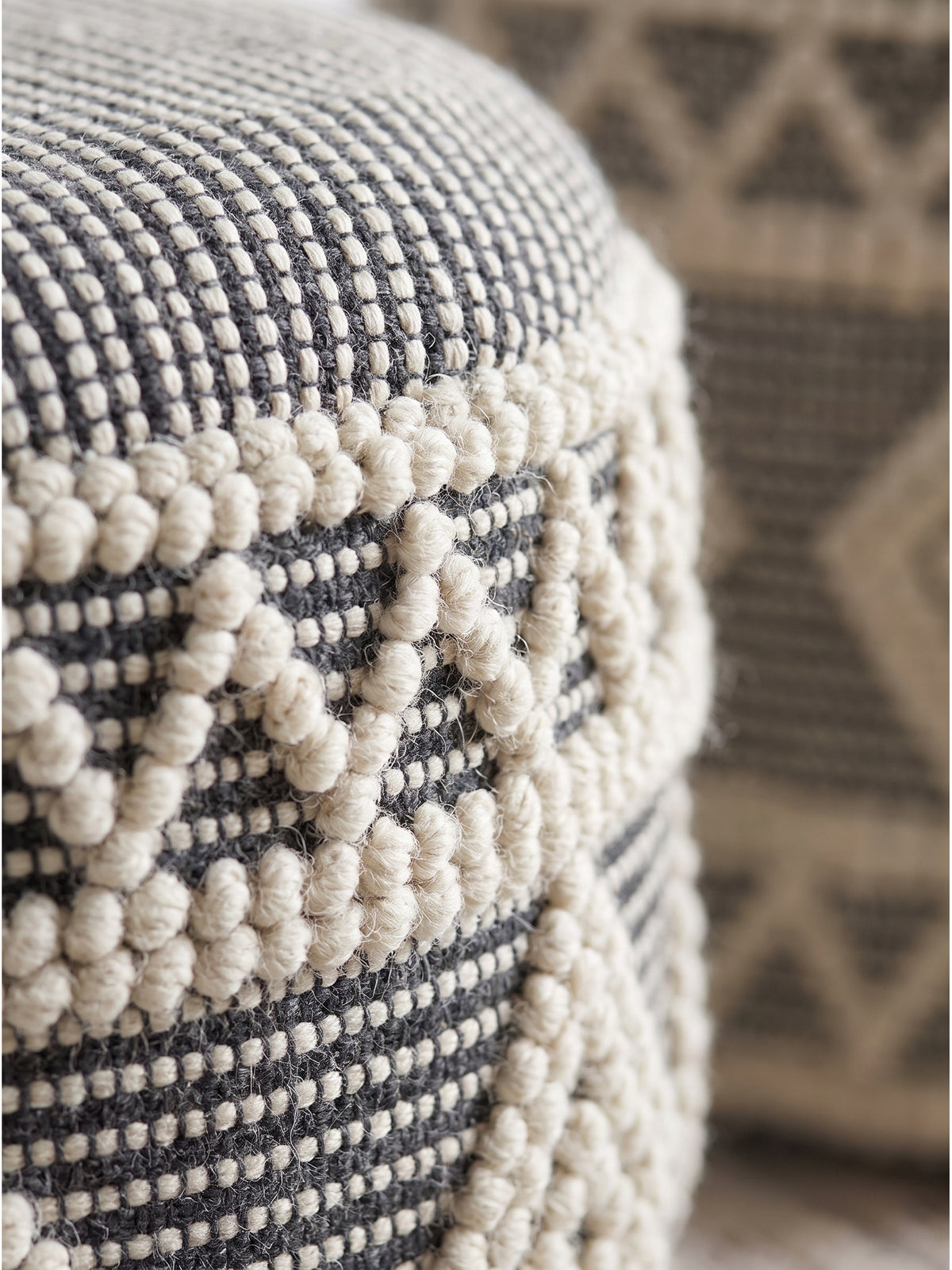 Nahaufnahme der getufteten Wollstruktur des runden Boho-Hockers mit geometrischem Muster aus dunklem und hellem Garn_