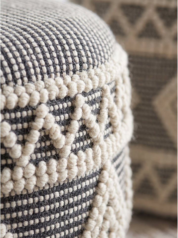 Nahaufnahme der getufteten Wollstruktur des runden Boho-Hockers mit geometrischem Muster aus dunklem und hellem Garn_