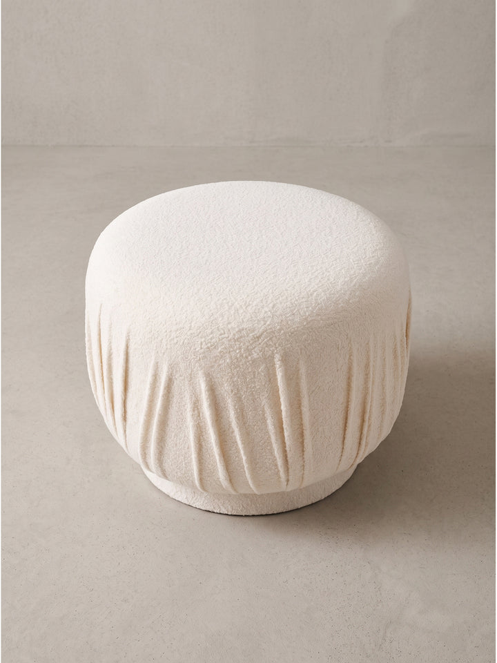Design Stoffhocker in Creme von schräg vorn mit sichtbarer Struktur des Bezugs und kompaktem Unterbau für gemütlichen Sitzkomfort_