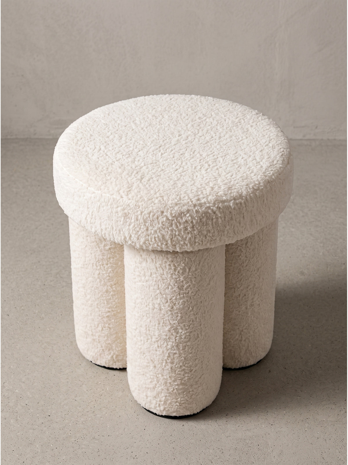 Design Stoffhocker in Creme schräg von vorn gesehen präsentiert die architektonische Struktur und weiche Polsterung im Studio