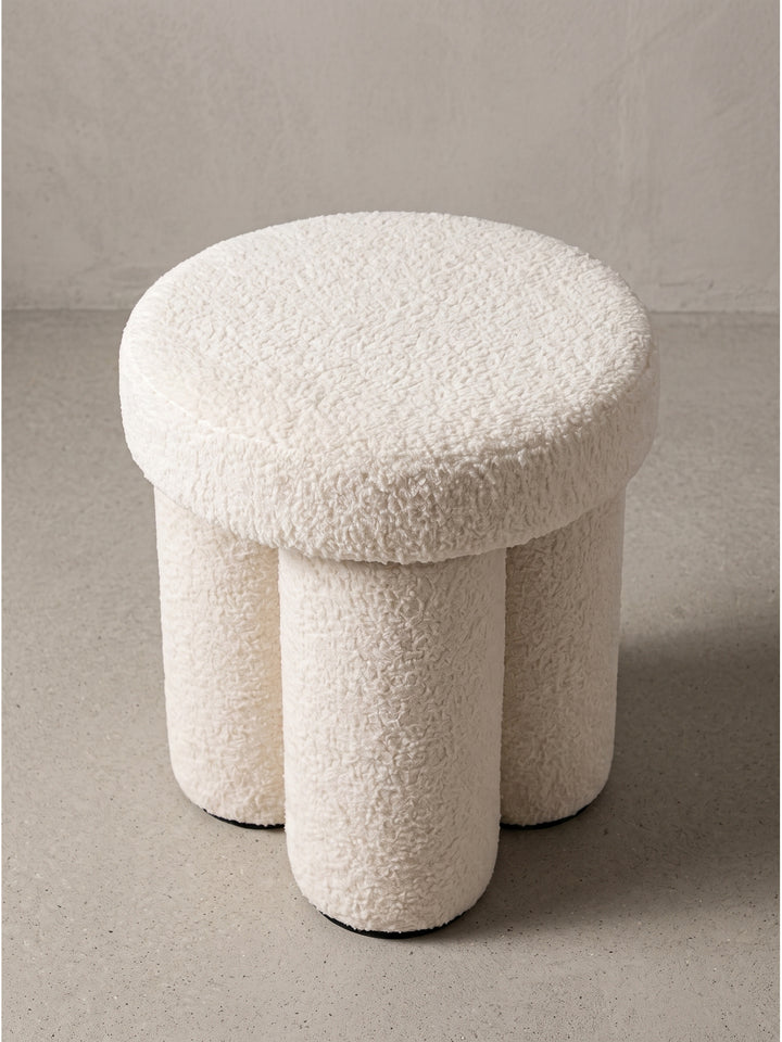 Design Stoffhocker in Creme schräg von vorn gesehen präsentiert die architektonische Struktur und weiche Polsterung im Studio_