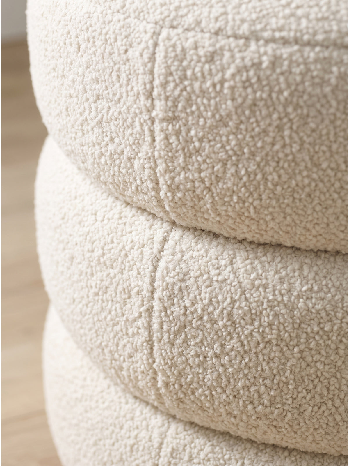 Detailaufnahme des cremefarbenen Teddy Stoffs am runden Polsterhocker mit sichtbarer flauschiger Struktur_