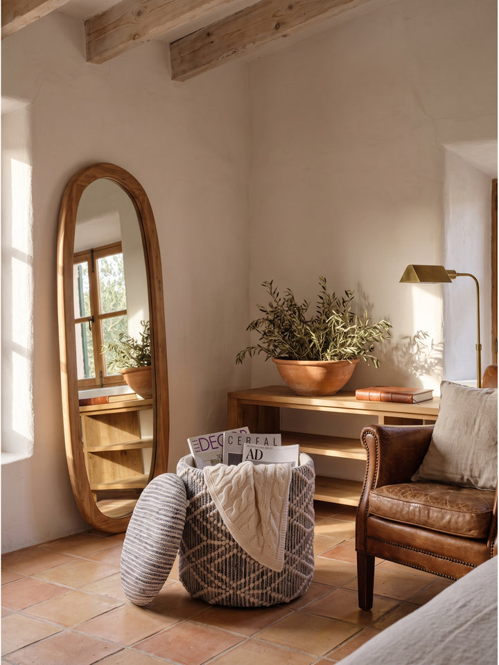 Runder Polsterhocker mit Stauraumfunktion neben einer minimalistischen Holzkonsole und einer Keramikleuchte im Boho-Stil_