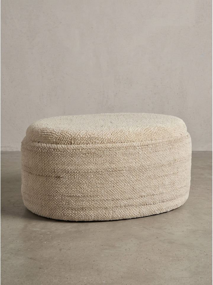 Ovaler Sitzhocker aus Wolle in Creme mit 81x62x40 cm vor weißem Hintergrund_