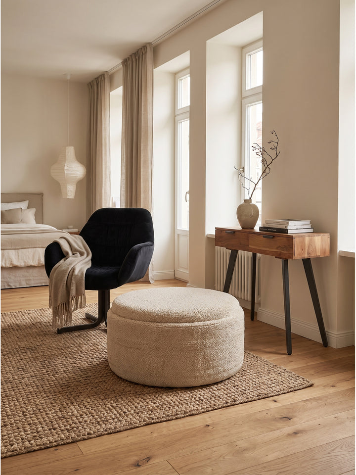 Cremefarbener Hocker als vielseitiger Couchtisch genutzt neben einem organisch geformten Lounge-Sessel_