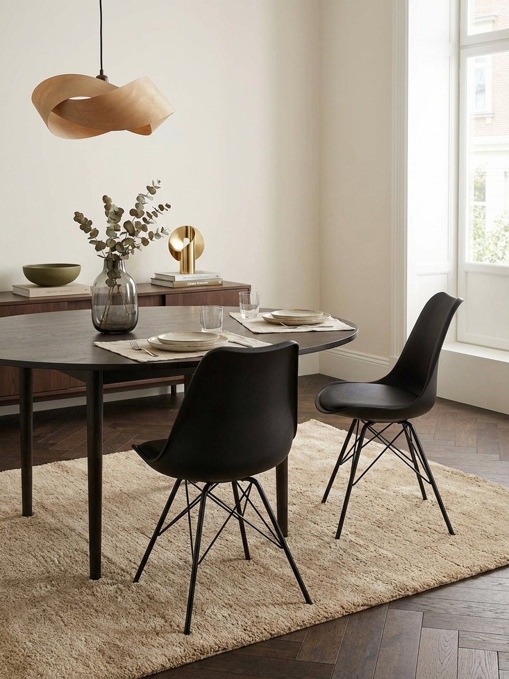 Schwarzer Esszimmerstuhl im skandinavischen Design in einem hellen, modernen Esszimmer, platziert an einem Tisch aus massivem Eichenholz auf einem beigen Wollteppich._