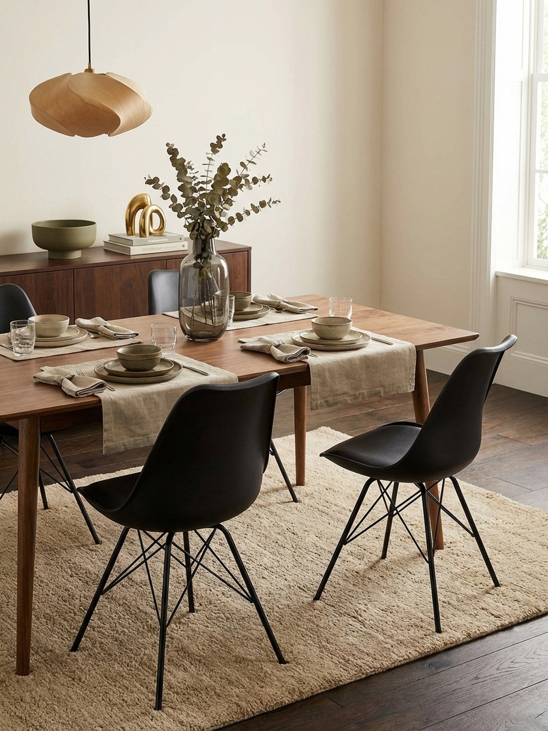 Draufsicht auf einen Essbereich mit vier schwarzen Schalenstühlen um einen runden Holztisch, die das klare Layout und die minimalistische Ästhetik des Raumes zeigt._