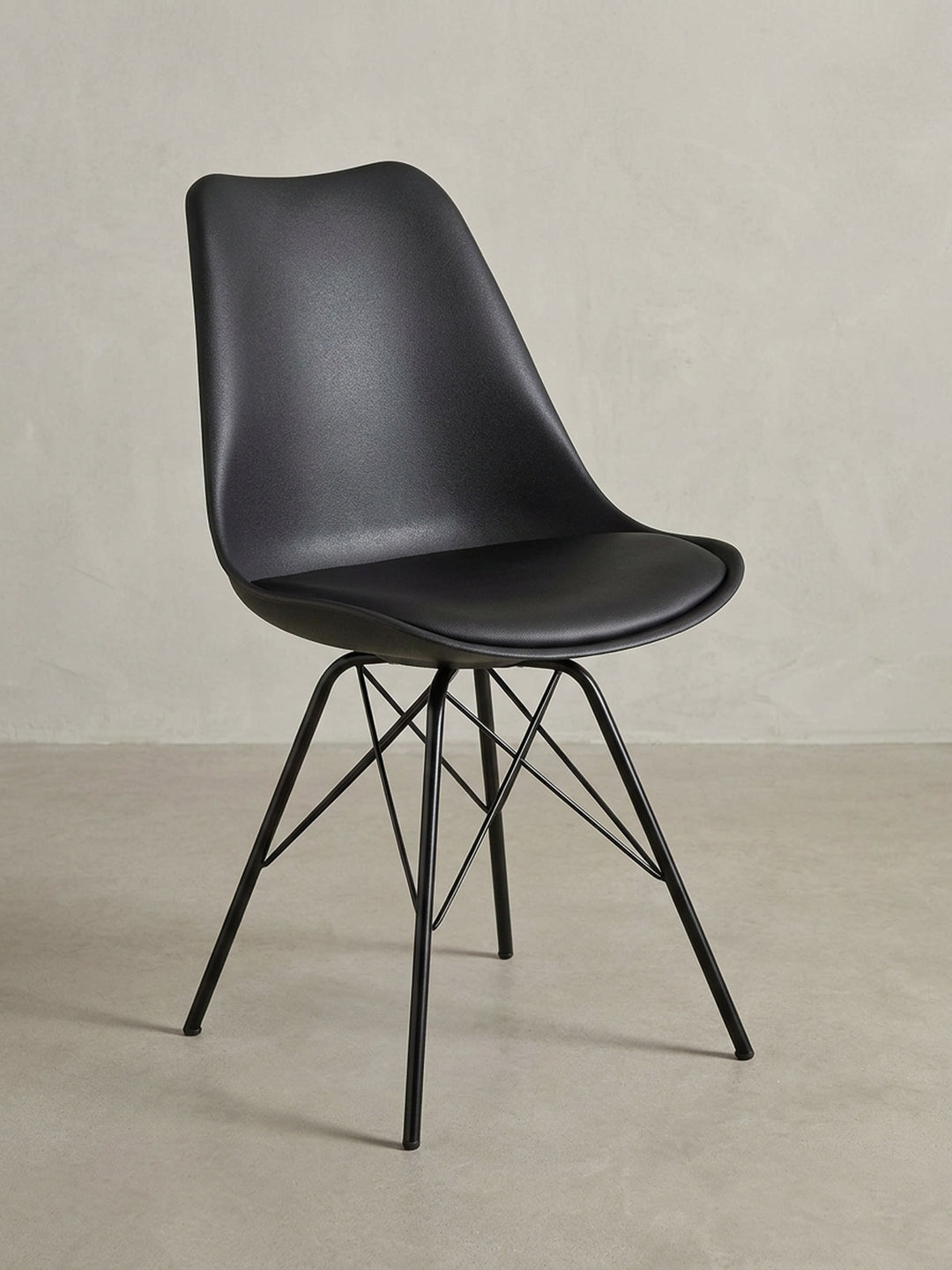 Seitenprofil des schwarzen Schalenstuhls, das die ergonomische Krümmung der Rückenlehne und die schräge Stellung der stabilen Eisenbeine betont. Stuhlhöhe 86 cm._