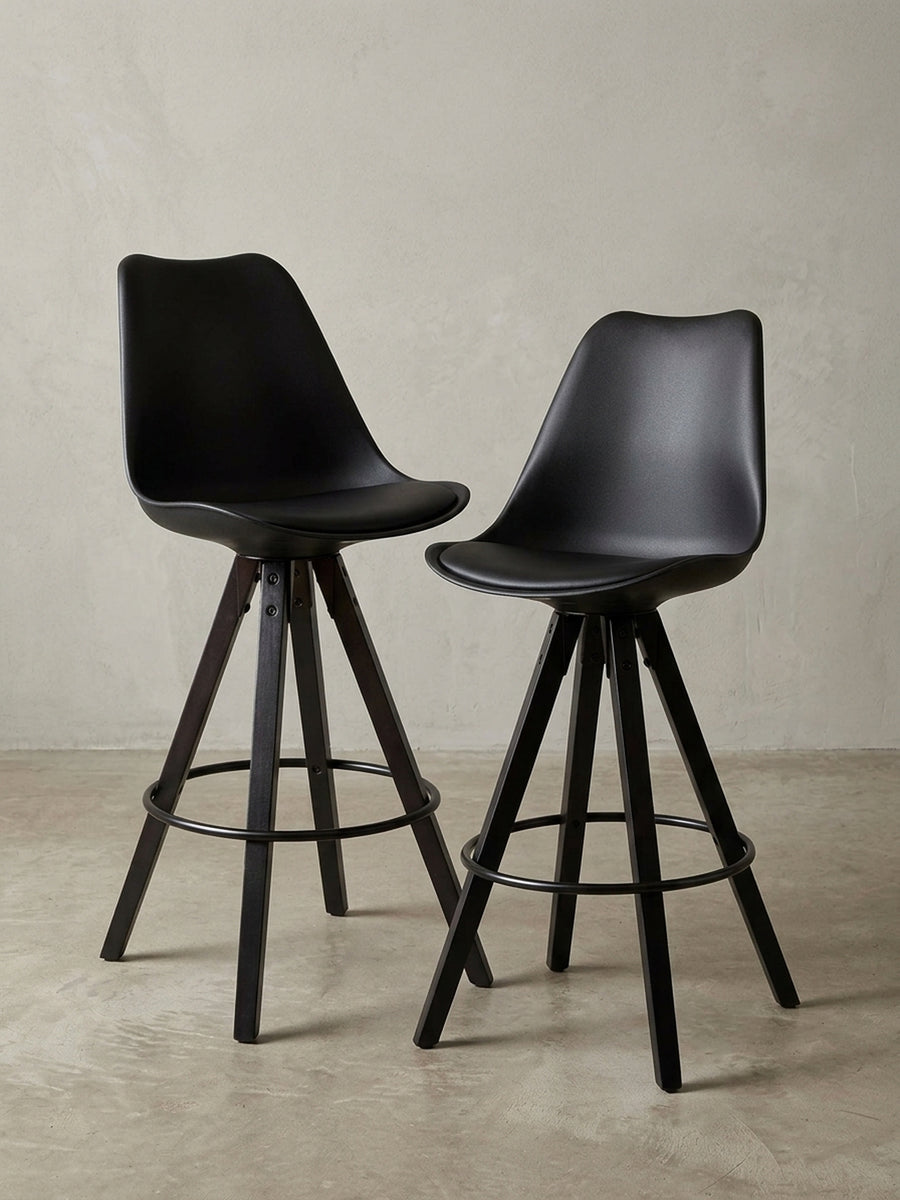 Design-Barhocker in Schwarz aus der Dreiviertelperspektive, die die organisch geformte Sitzschale und die stabile Konstruktion der Holzbeine zeigt._