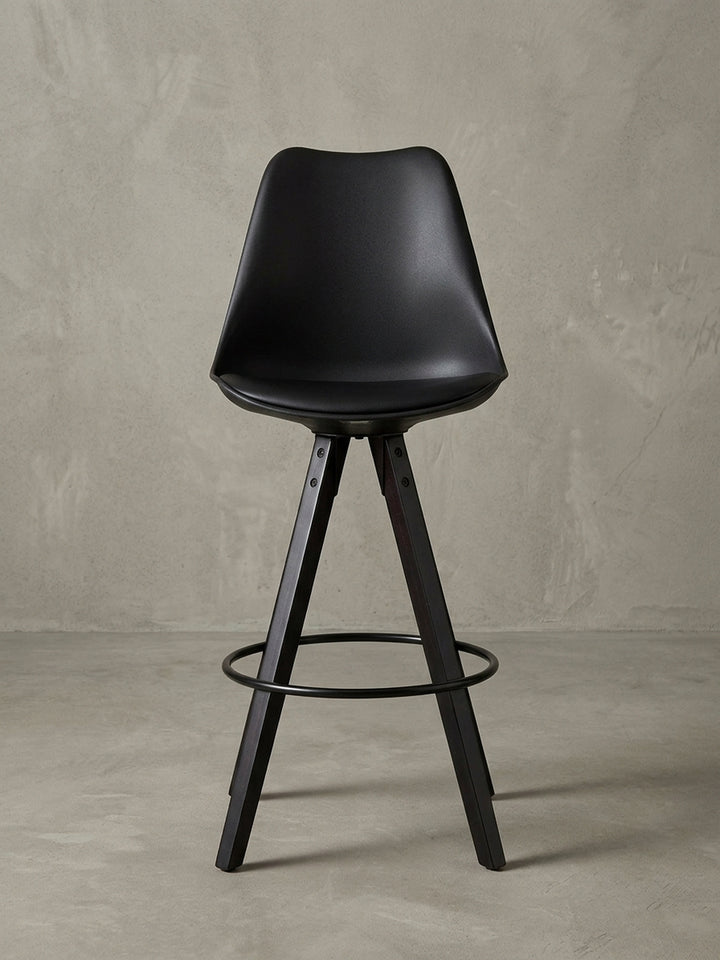 Seitenprofil eines schwarzen Tresenhockers mit hoher Lehne und elegant gespreizten Holzbeinen, ideal für Küchentheken mit 77 cm Sitzhöhe._