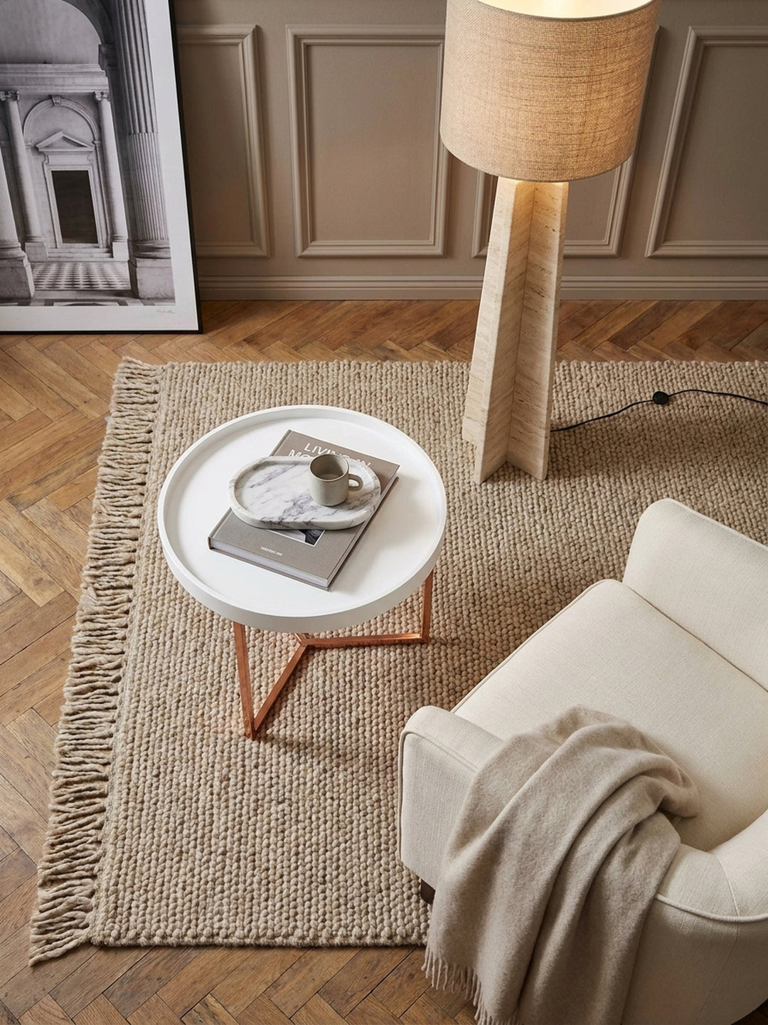 Draufsicht auf den runden Tabletttisch mit abnehmbarer Ablagefläche neben einem beigefarbenen Sofa im modern eingerichteten Lounge-Bereich_
