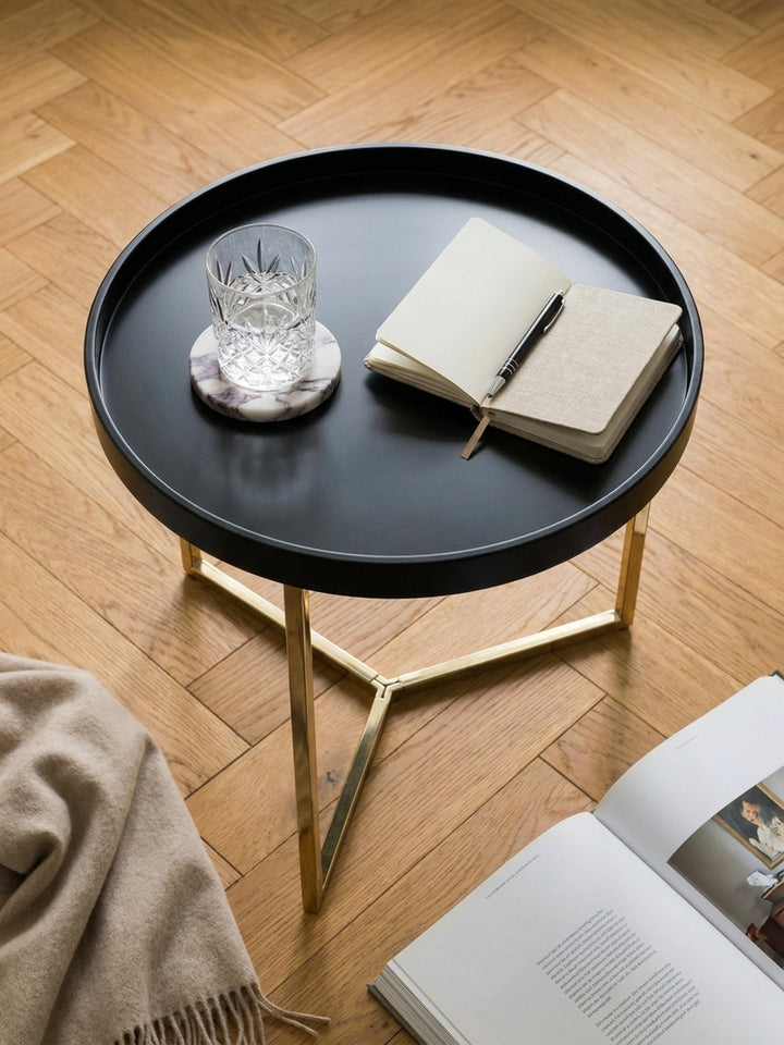 Runder Tabletttisch 58x42 cm mit goldfarbenem Gestell von oben betrachtet auf einem hellen Vintage-Teppich neben einem beigefarbenen Leinensessel._