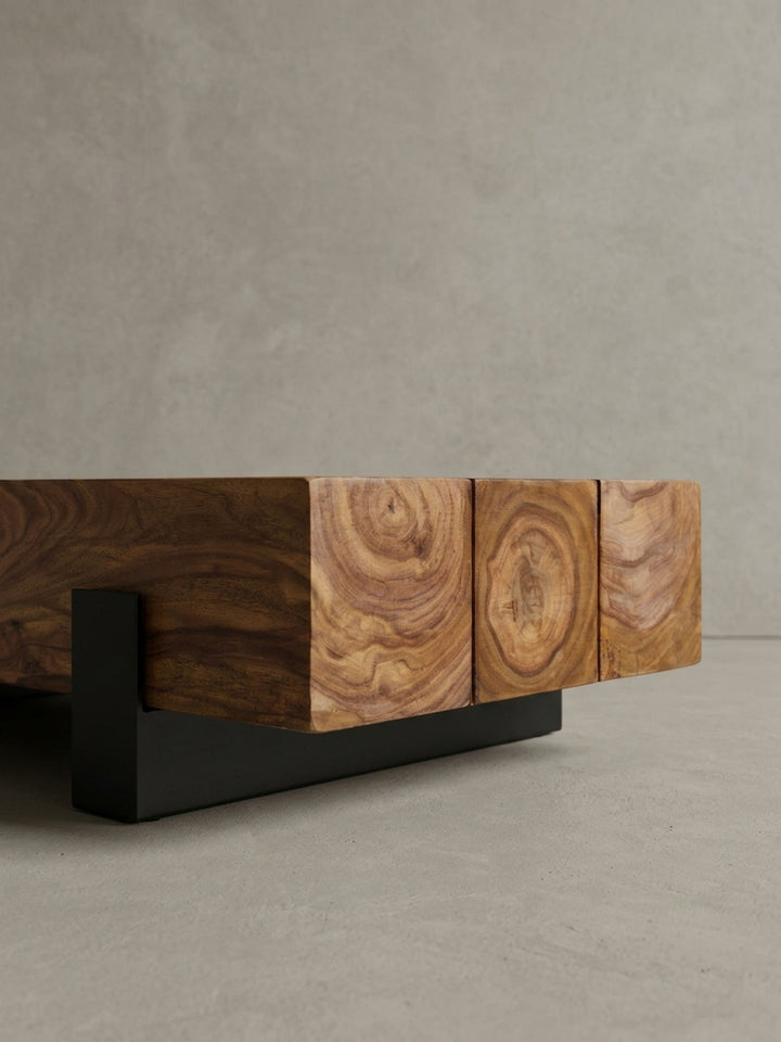 Nahaufnahme des Fußgestells am Massivholz Wohnzimmertisch. Der Kontrast zwischen der lebendigen Holzmaserung und den minimalistischen, 7cm hohen schwarzen Metallkufen steht im Fokus._