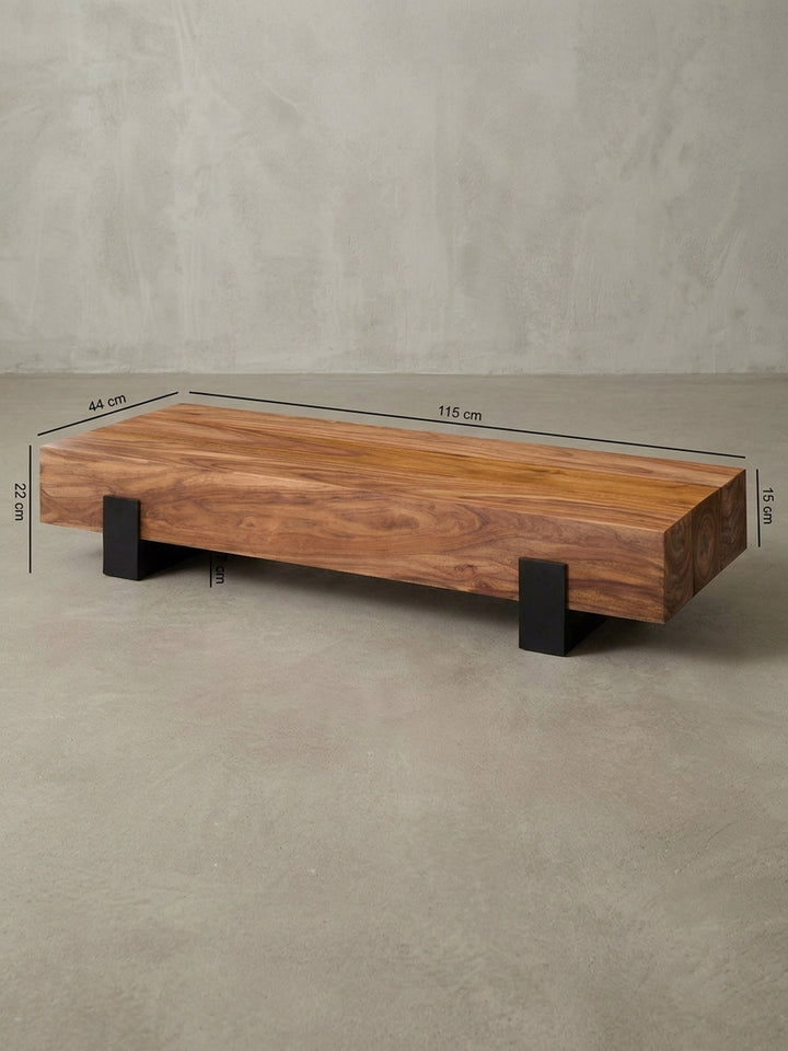 Detailansicht der Rückseite des rechteckigen Stubentisches. Stabile Konstruktion des 115x44cm Holzblocks mit nahtlosem Übergang zu den bodennahen schwarzen Metallstützen des Gestells._