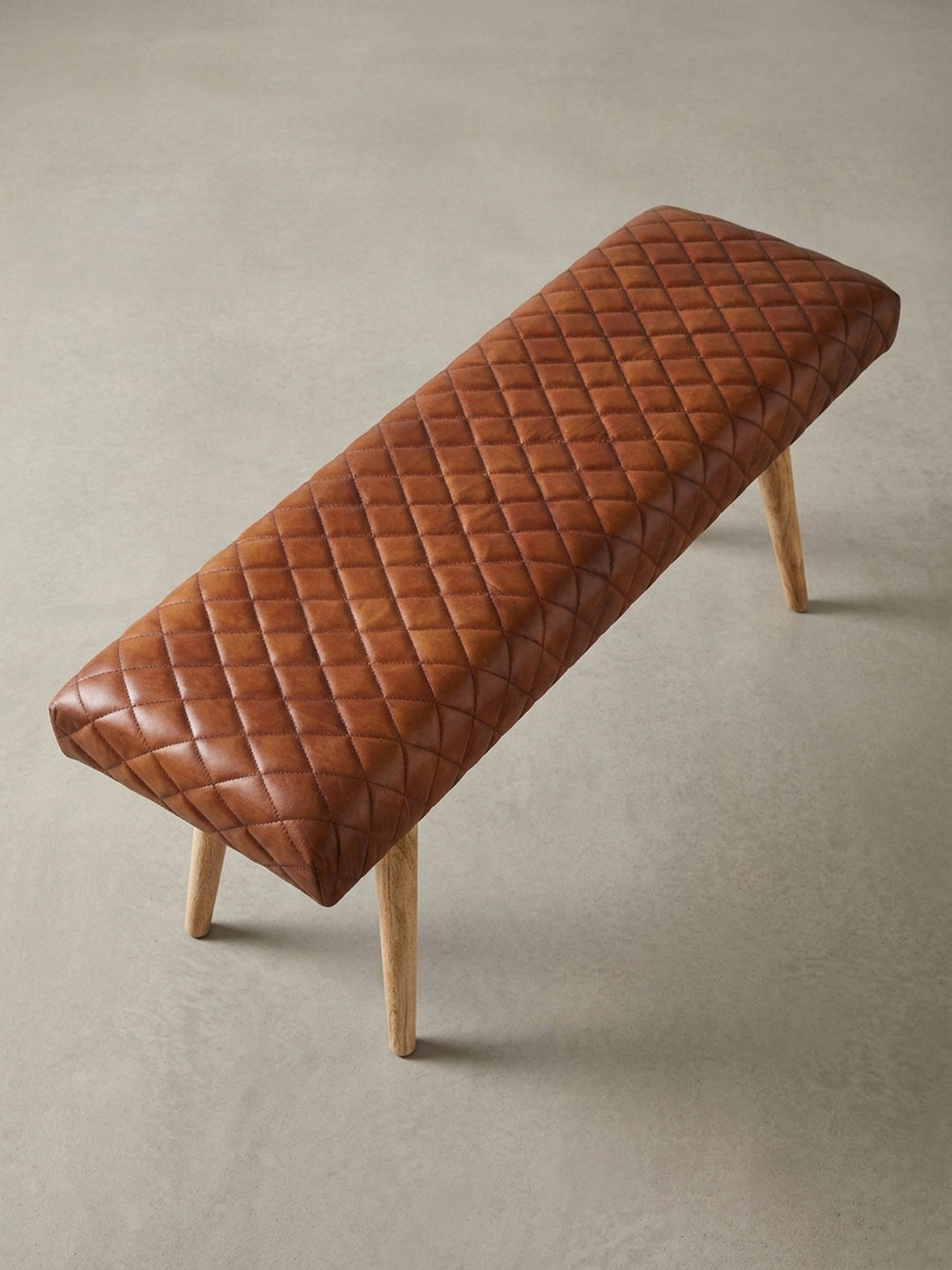 Alternative Perspektive der Lederbank, die das Zusammenspiel von der warmen braunen Sitzfläche und dem hellen, naturbelassenen Mangoholz der Beine zeigt._