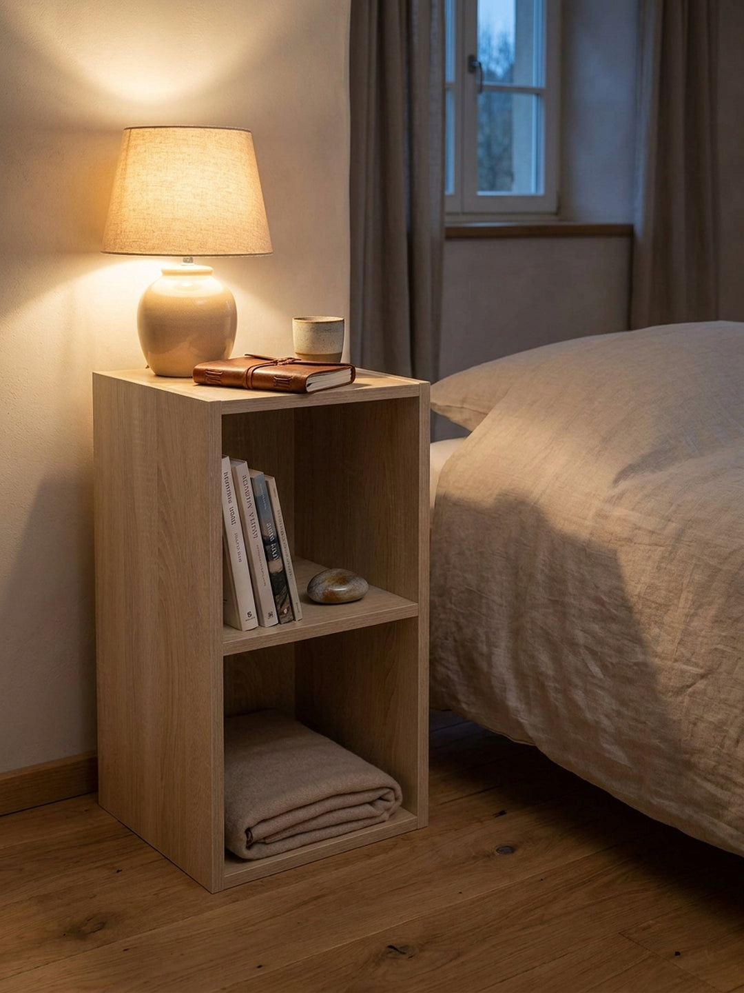 Dekoriertes kleines Bücherregal in heller Holznachbildung mit gestapelten Leinen-Bildbänden und einer minimalistischen Keramikvase im sonnendurchfluteten Raum._