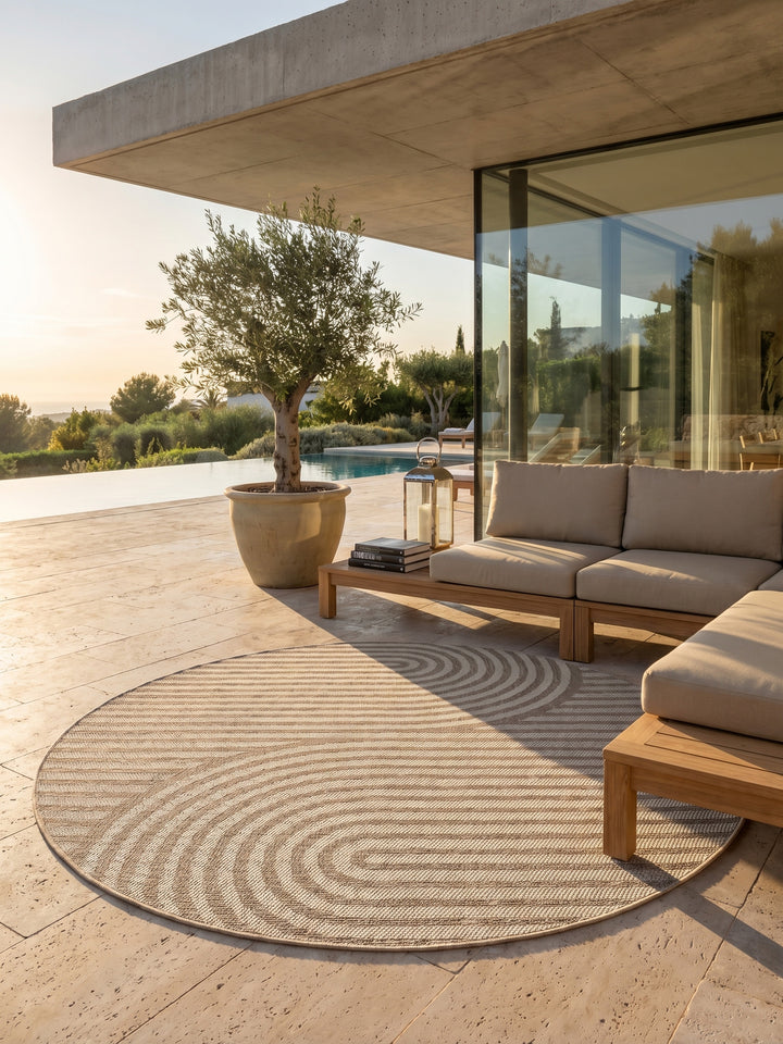 Runder beiger Boho-Teppich auf einer sonnigen Terrasse mit Rattanmöbeln und Terrakotta-Töpfen._