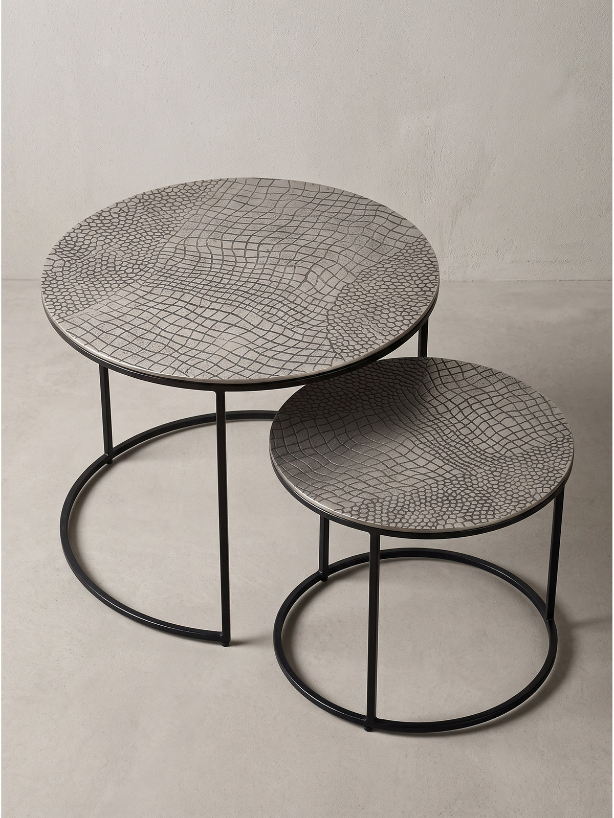 Zwei ineinandergeschobene Beistelltische aus Eisen zeigen ihre asymmetrische Anordnung und das klare Design in Schwarz und Silber._
