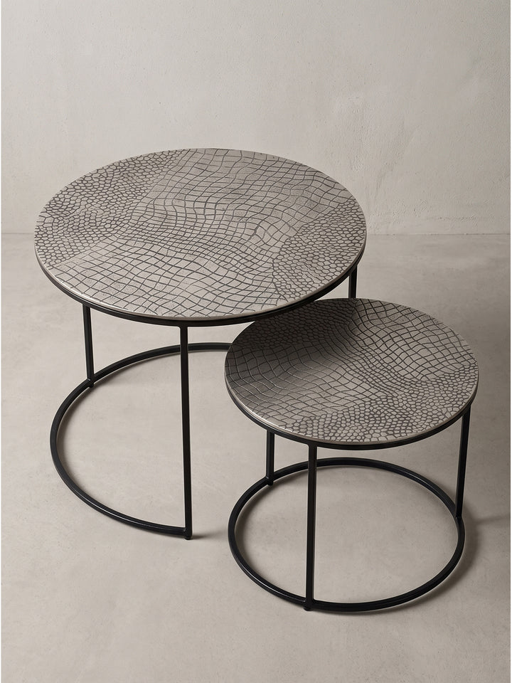 Zwei ineinandergeschobene Beistelltische aus Eisen zeigen ihre asymmetrische Anordnung und das klare Design in Schwarz und Silber._