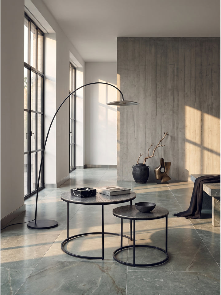 Runder Couchtisch aus silbernem Aluminium im 2er Set als Zentrum eines minimalistischen Wohnzimmers auf großformatigem Kalksteinboden._