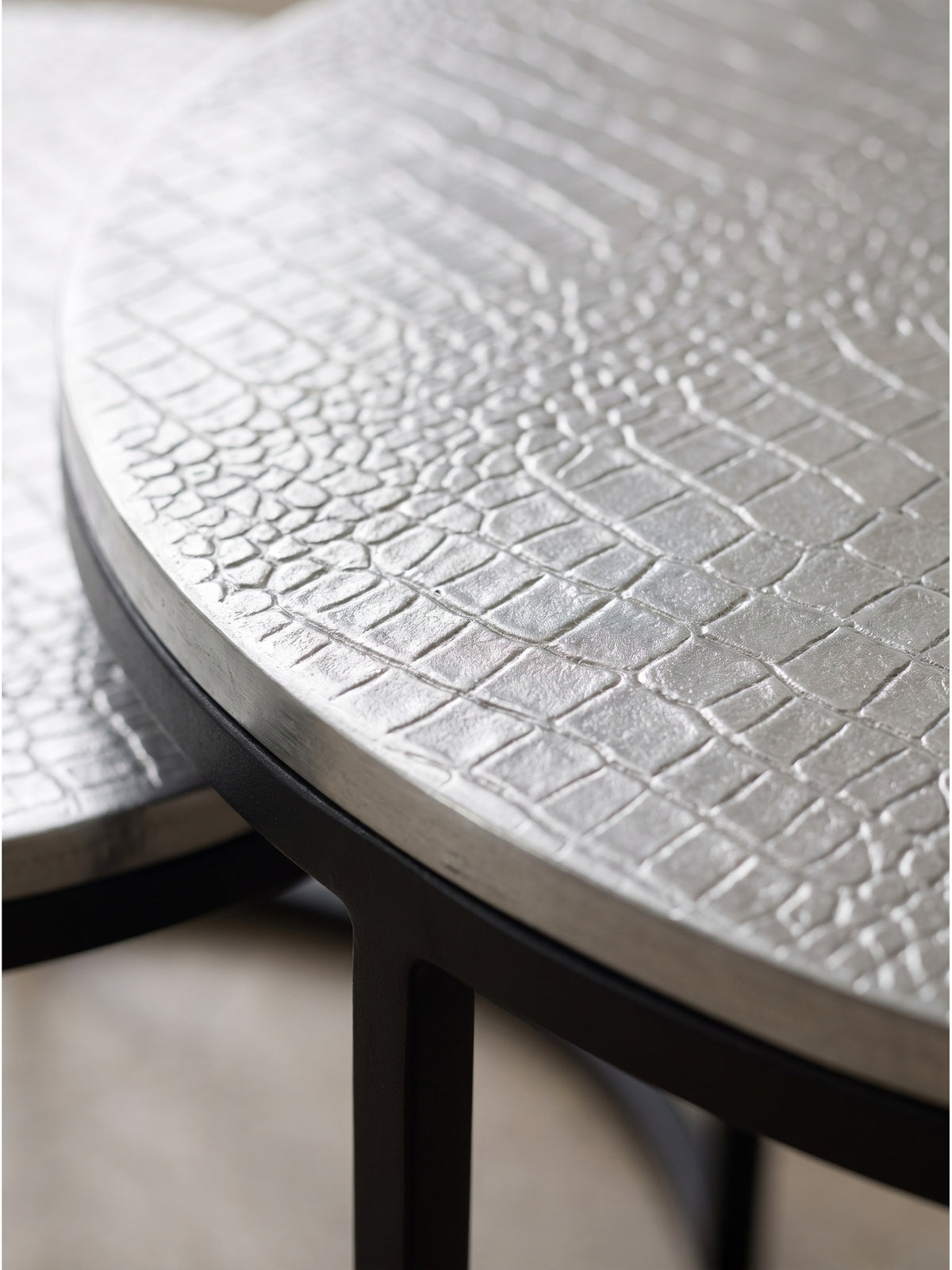 Detaillierte Prägung auf der silbernen Aluminiumplatte des Wohnzimmertisches neben einem dunklen eisernen runden Gestell._