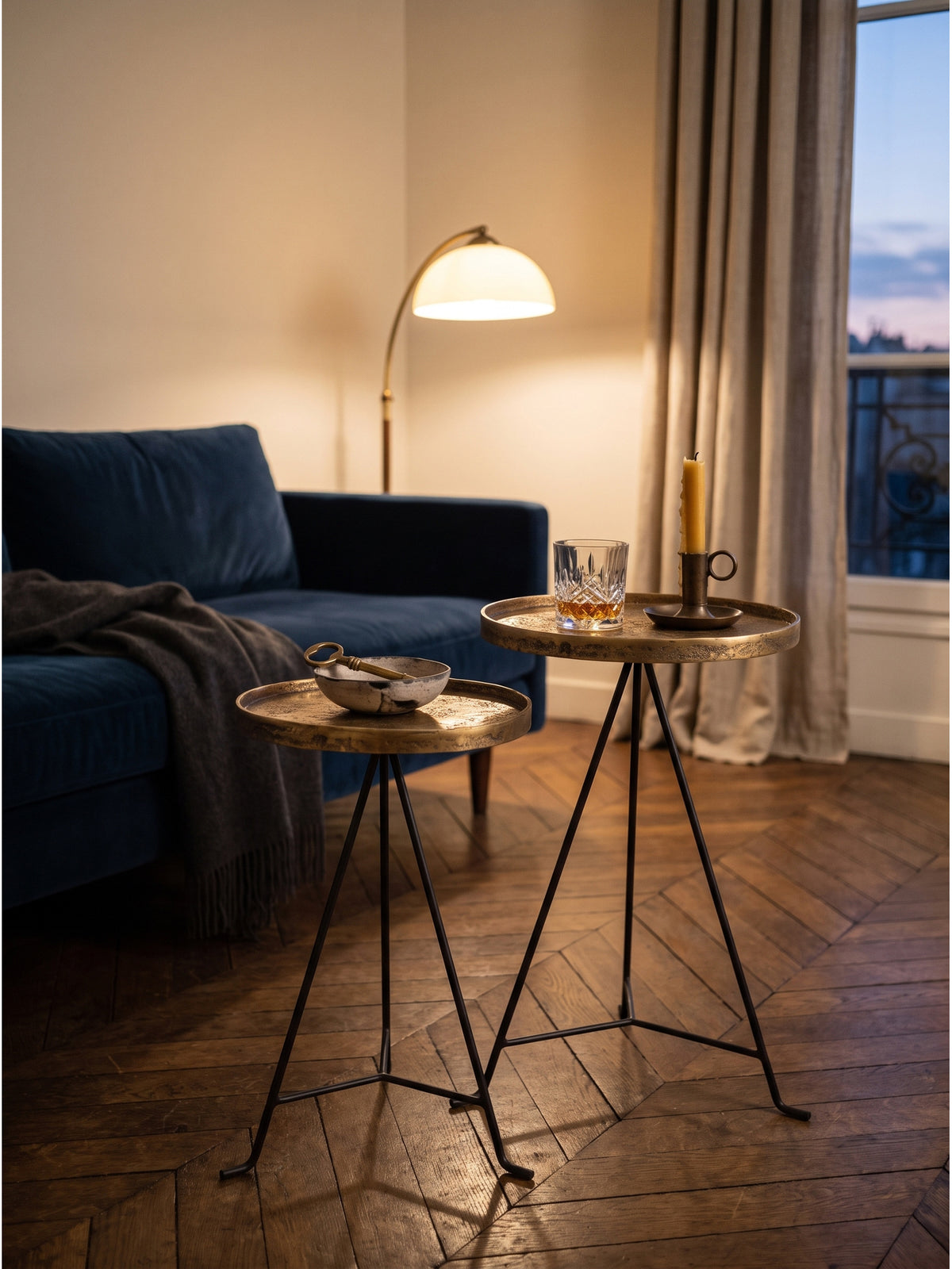Ein Kristallglas und eine Bienenwachskerze auf dem goldenen Metalltisch im warmen Licht einer Leinen-Stehlampe arrangiert._