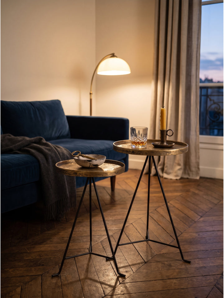 Ein Kristallglas und eine Bienenwachskerze auf dem goldenen Metalltisch im warmen Licht einer Leinen-Stehlampe arrangiert._