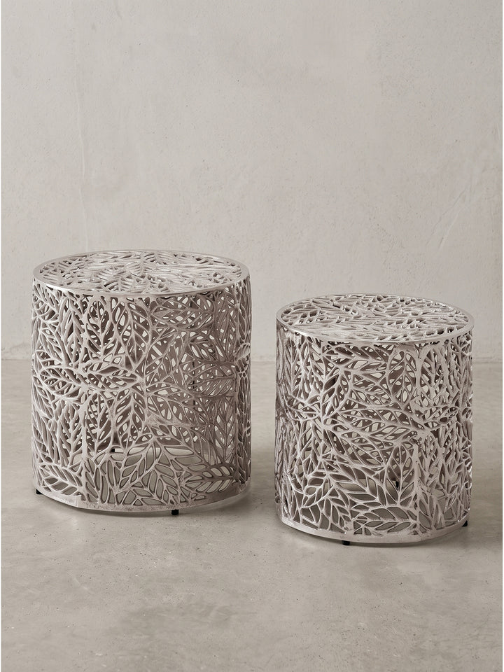 Zwei runde Satztische aus Aluminium in Silber mit durchbrochenem Blattmuster vor neutralem Hintergrund_