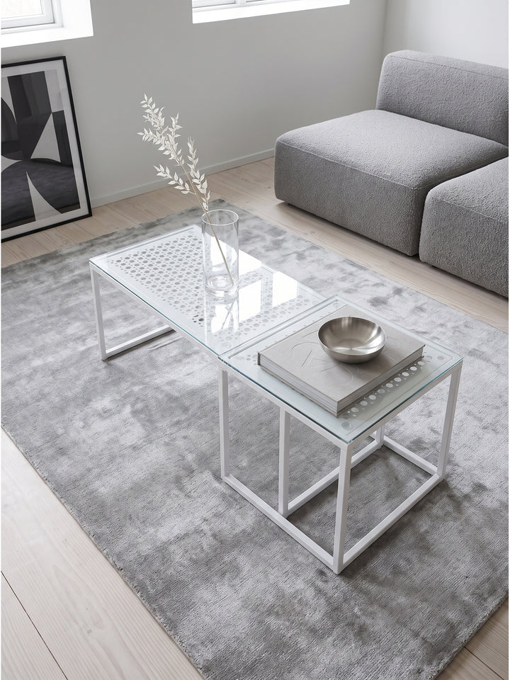 Geometrischer Couchtisch von oben betrachtet mit Sicht auf das dekorative Lochmuster unter der Glasplatte neben einem Bouclé Sofa_