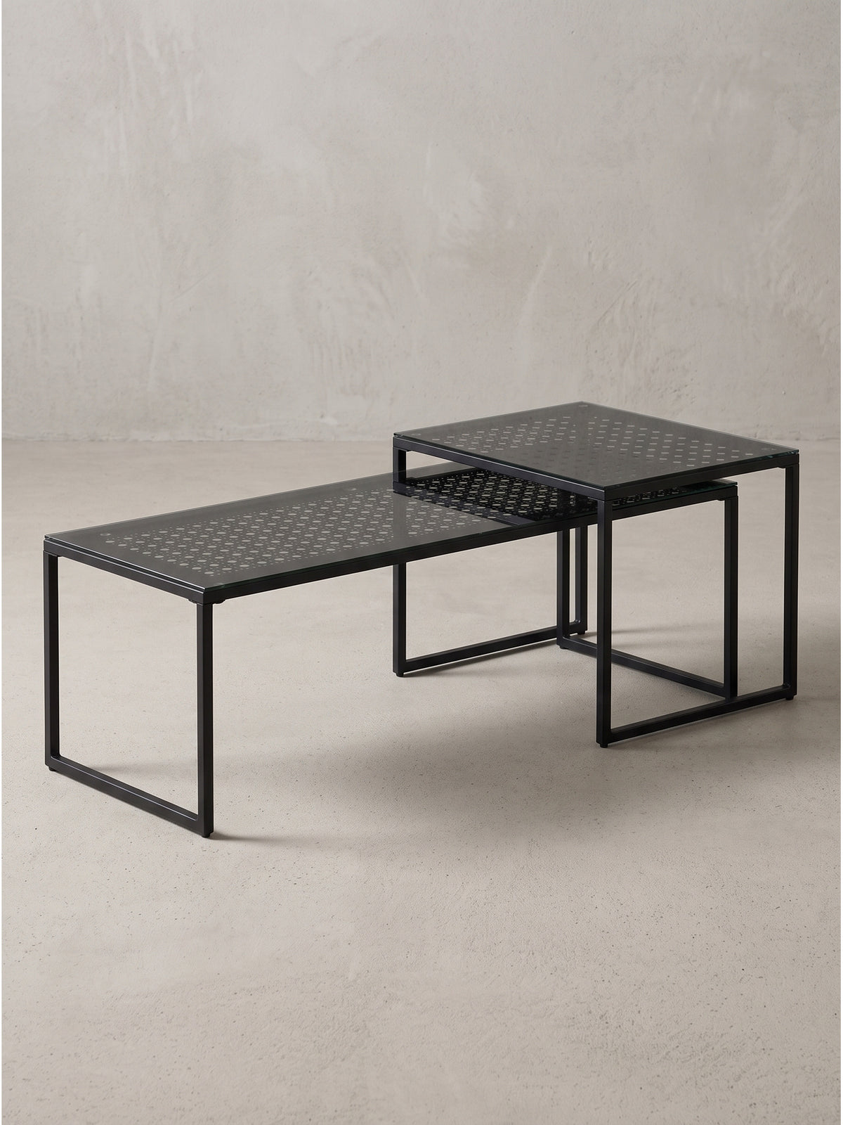 Vollflächige Ansicht des ineinandergeschobenen Satztisch Sets aus schwarzem Metall und Glas vor neutralem weißen Hintergrund._