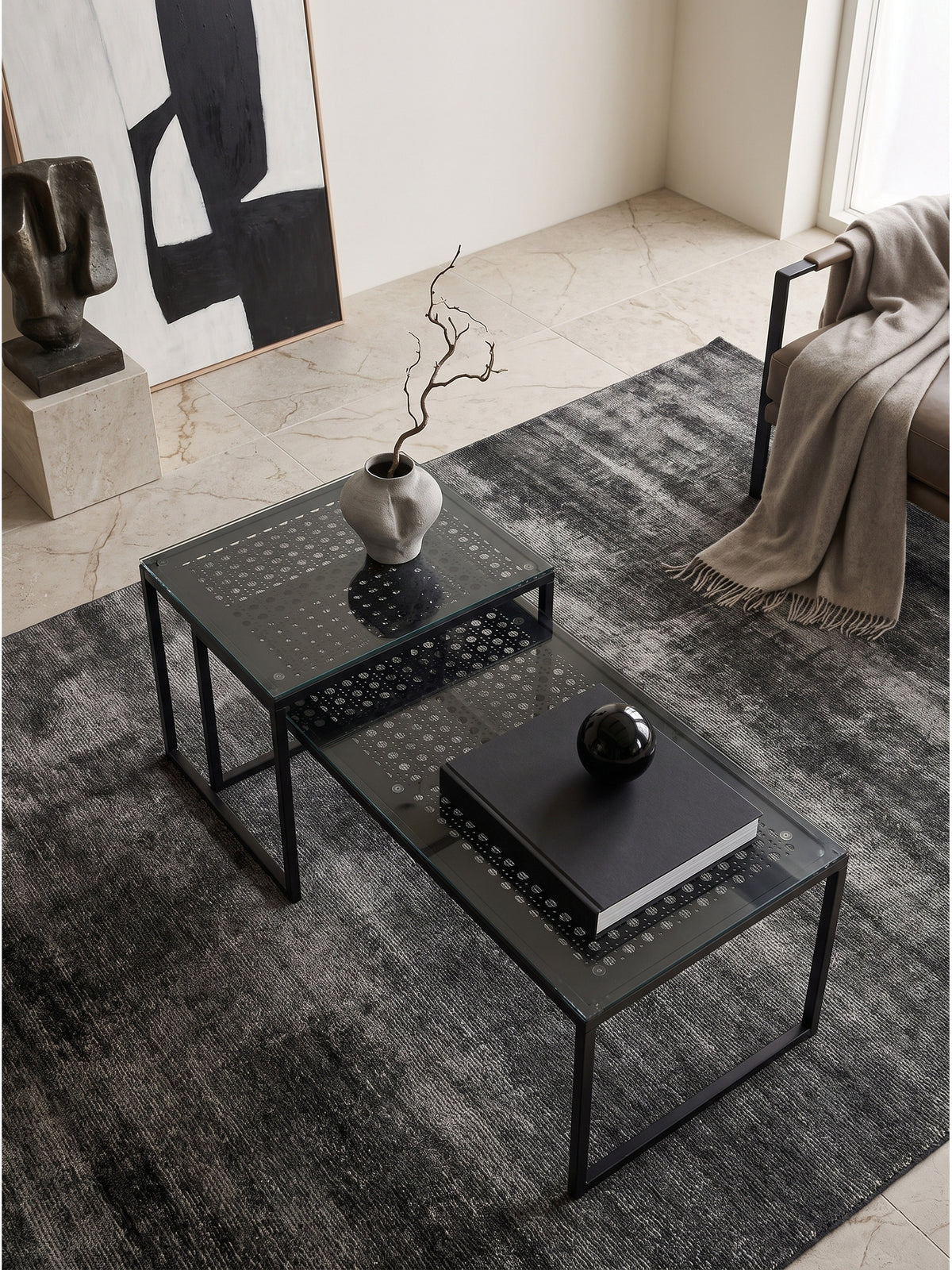 Geometrischer Couchtisch mit bedruckter Glasplatte in einem minimalistischen Loft von oben betrachtet auf silbernem Seidenteppich._