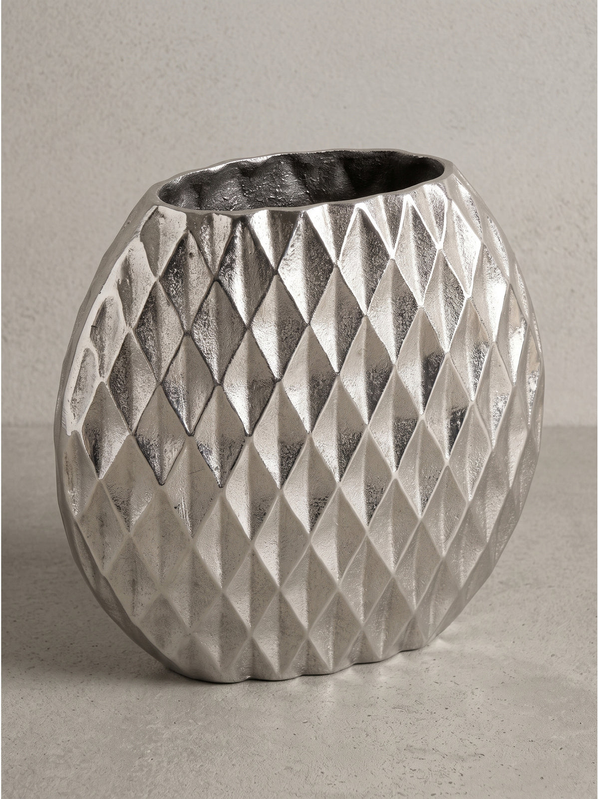 Detailansicht der markanten Rautenstruktur auf der kühlen Oberfläche der silbernen Aluminium-Vase im modernen Design._