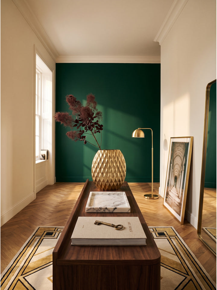 Große goldene Tischvase aus Aluminium mit Rautenstruktur im luxuriösen Art-Deco-Wohnzimmer auf einem Walnuss-Konsolentisch vor smaragdgrüner Wand._
