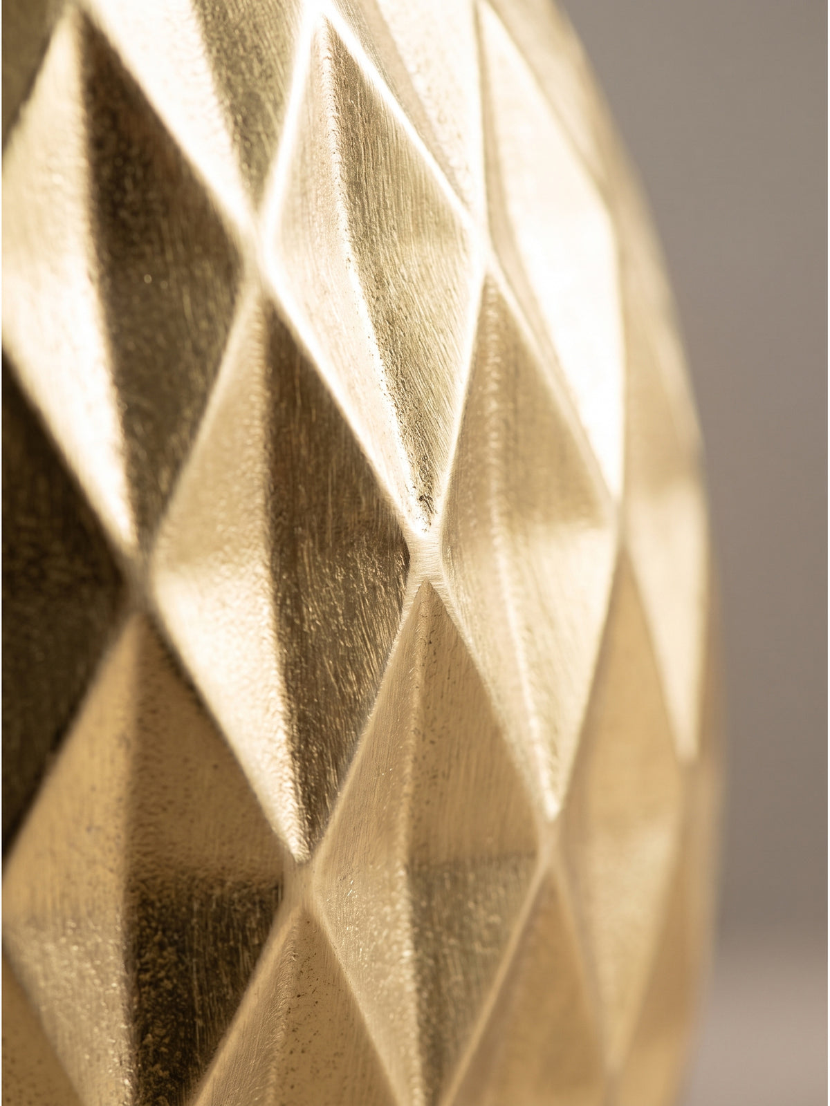 Nahaufnahme der markanten Rautenstruktur der handgefertigten Tischvase aus Aluminium, deren glänzende Oberfläche das Licht sanft bricht._