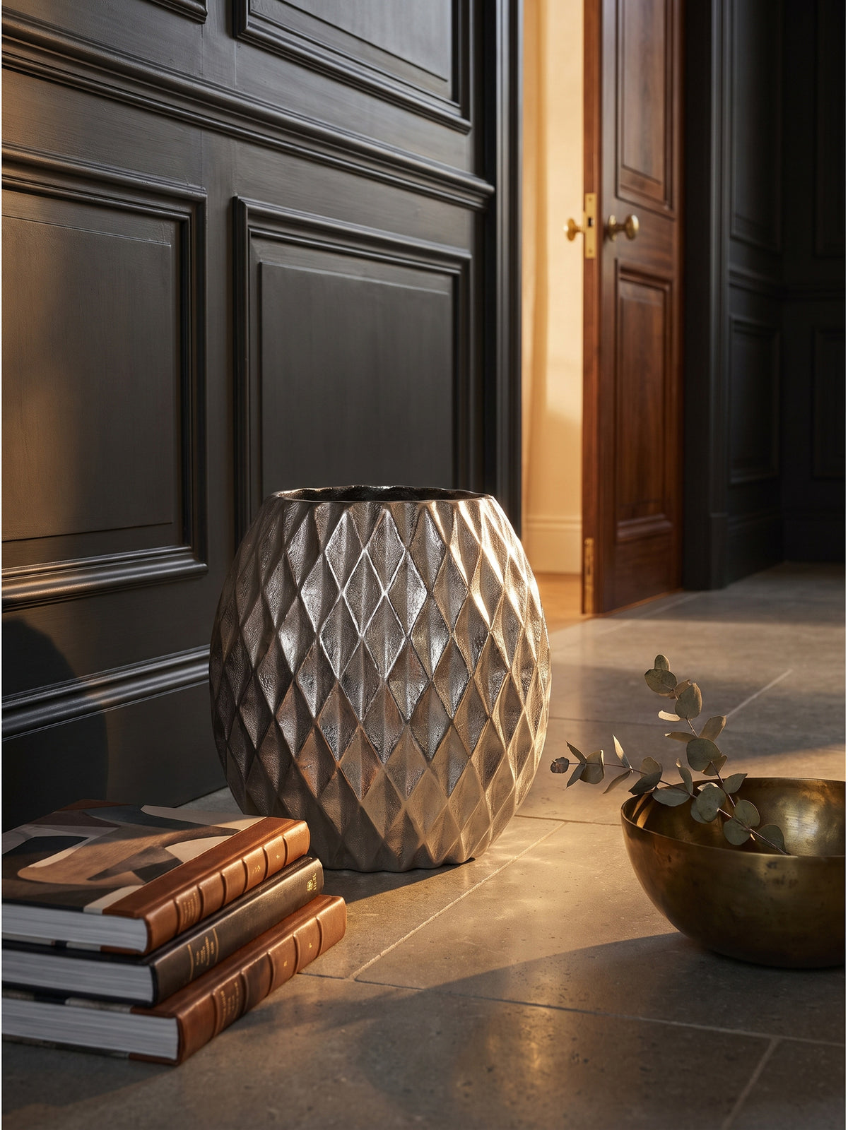 Silberne Design-Vase aus massivem Alu mit getrocknetem Eukalyptus arrangiert, daneben ein rauer Obsidianstein auf dunklem Untergrund._