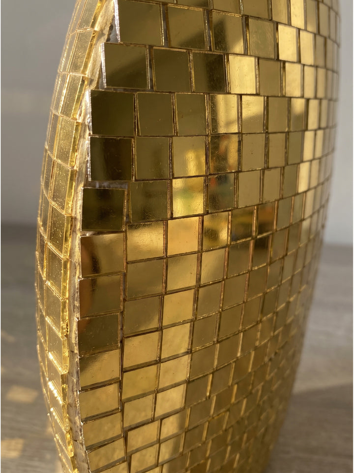 Nahaufnahme der funkelnden goldenen Mosaik-Quadrate auf dem Eisenkorpus der handgefertigten Dekovase mit intensiver Lichtreflexion_