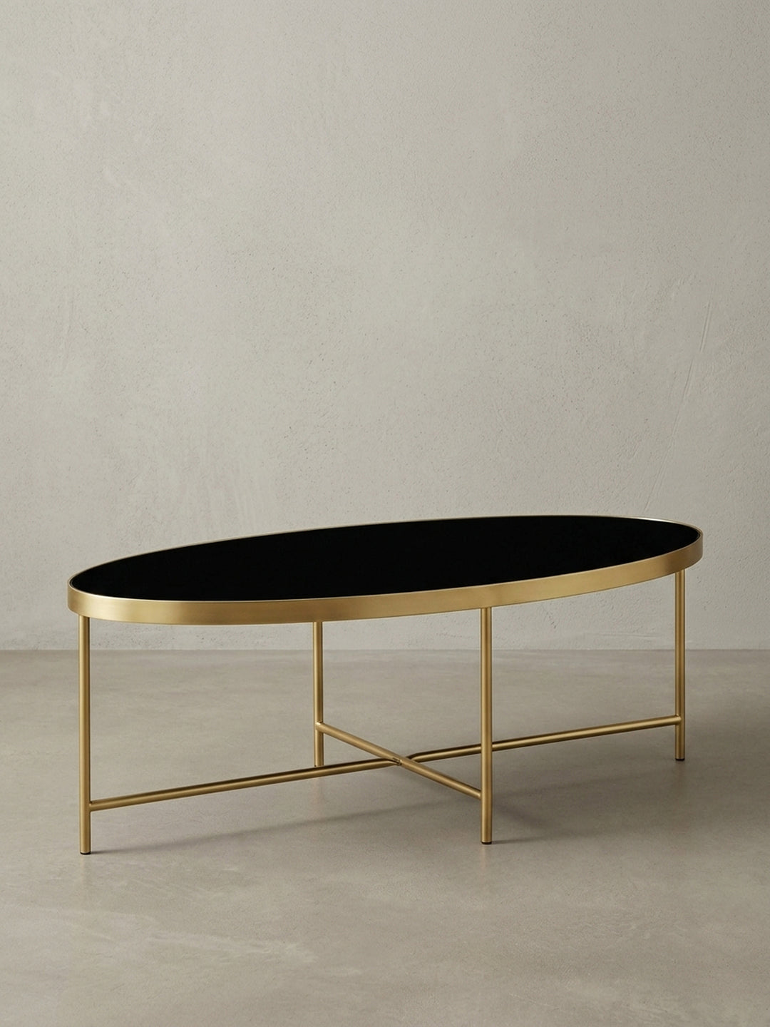 Moderner Lounge Tisch in ovaler Form aus der Dreiviertelperspektive, das gekreuzte Untergestell aus mattgoldenem Stahl ist unter der Glasplatte gut erkennbar._