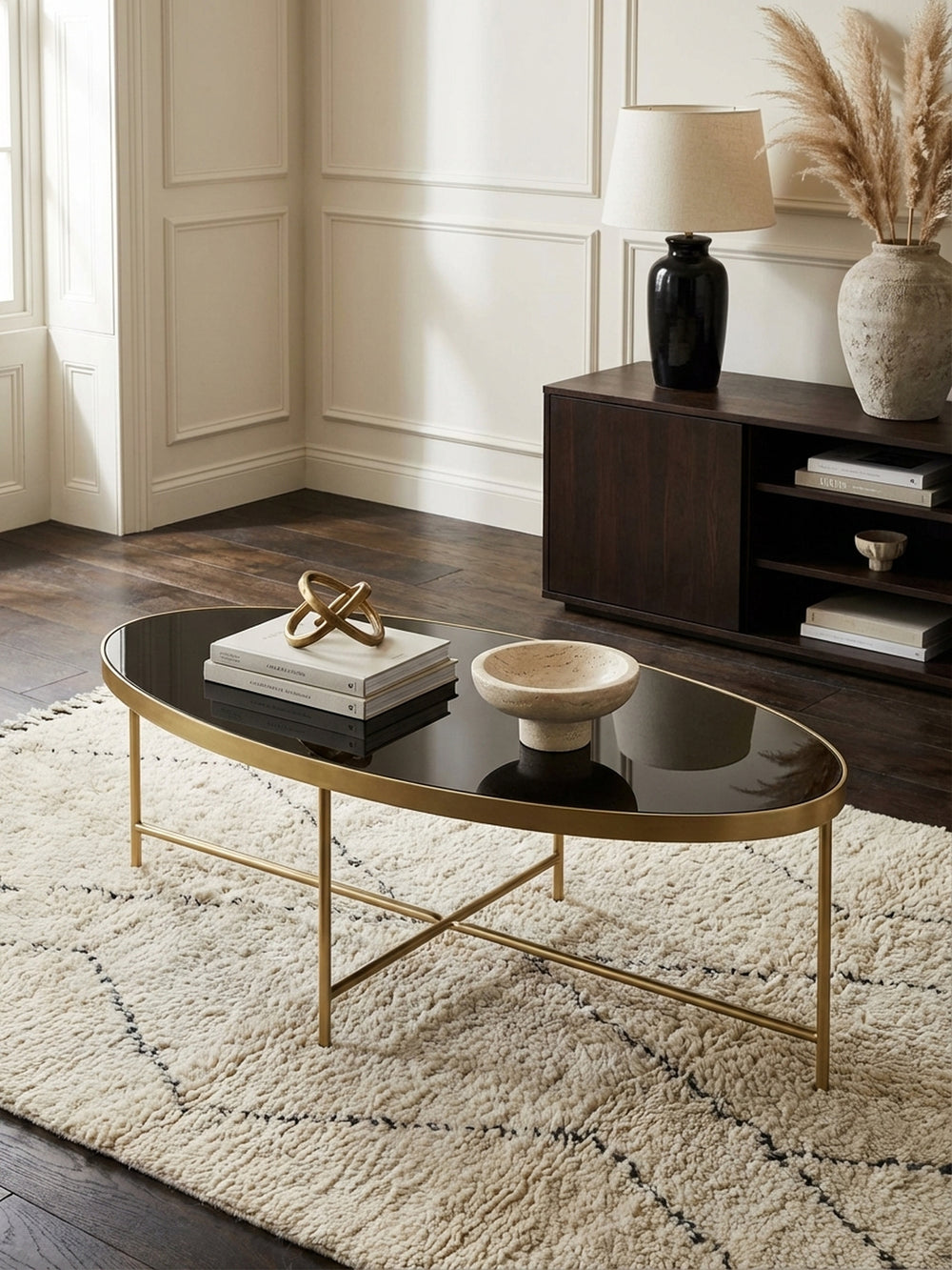 Design Couchtisch oval von oben fotografiert, die glänzende schwarze Glasoberfläche und das filigrane goldene Metallgestell kommen auf dem grauen Teppich zur Geltung._