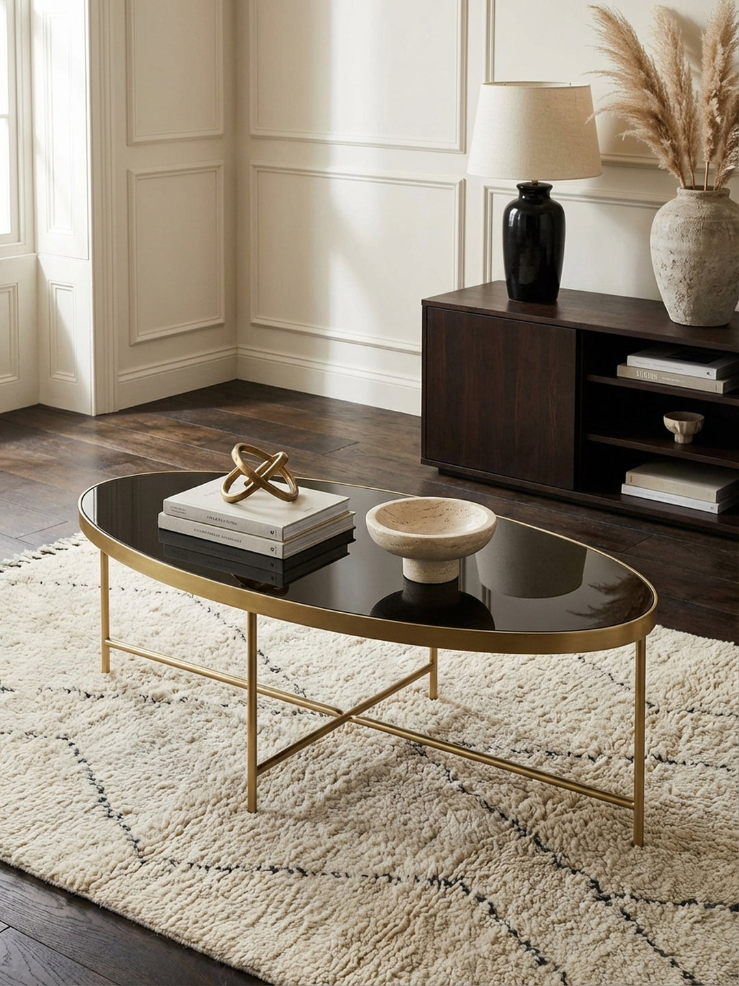 Design Couchtisch oval von oben fotografiert, die glänzende schwarze Glasoberfläche und das filigrane goldene Metallgestell kommen auf dem grauen Teppich zur Geltung._