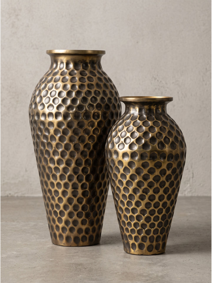 Profilansicht der Deko Vase aus Aluminium in Gold mit bauchiger Silhouette auf einem hellen Vintage-Teppich_