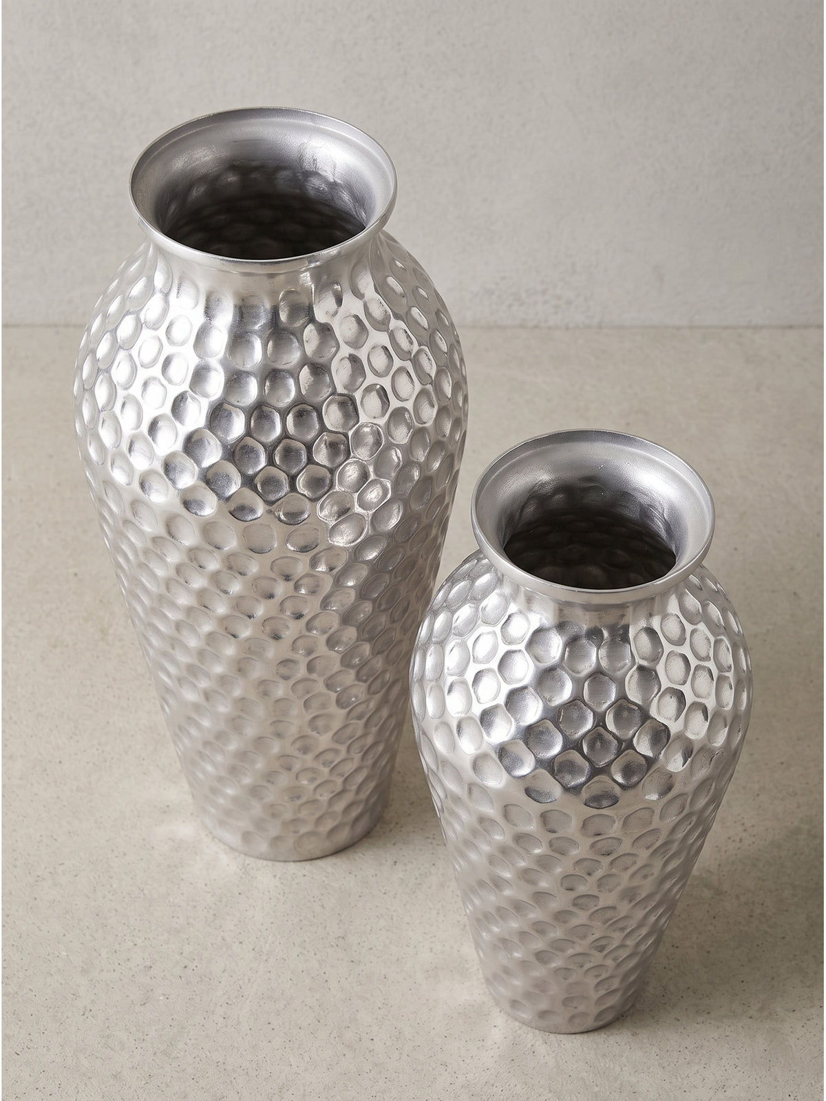 Leicht seitliche Perspektive der bauchigen silbernen Metallvasen mit schmalem Hals, welche die reflektierende Oberflächenstruktur deutlich zeigt._