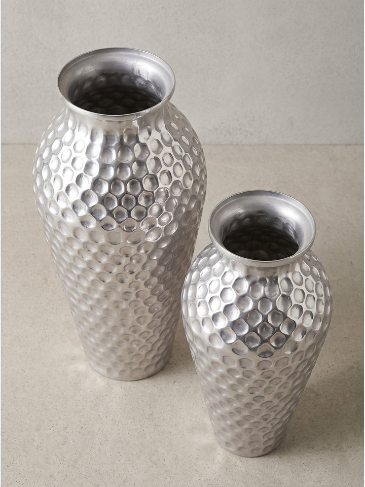 Leicht seitliche Perspektive der bauchigen silbernen Metallvasen mit schmalem Hals, welche die reflektierende Oberflächenstruktur deutlich zeigt._