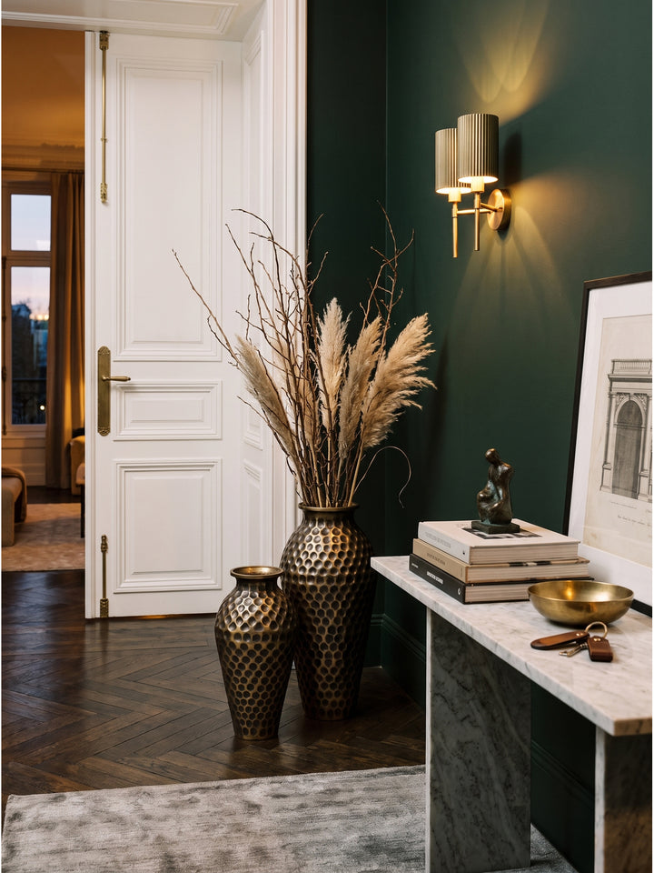 Goldene Deko Vase aus Aluminium dekoriert mit getrockneten Olivenzweigen neben einem Kunstband auf dem Boden_