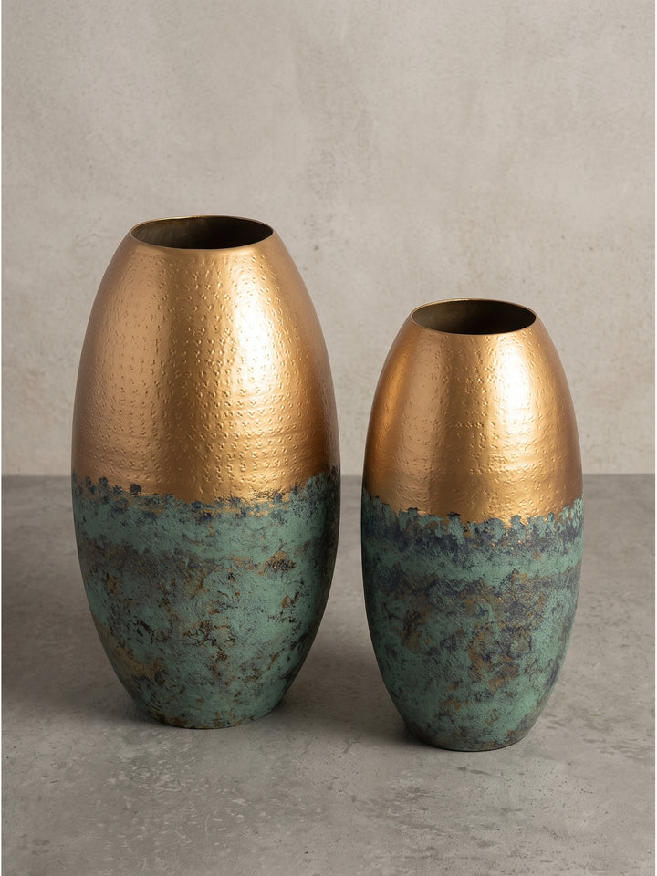 Makro-Detail des glatten Übergangs von der fein ziselierten goldenen Oberfläche zur rustikalen türkisgrünen oxidierten Patina der schweren Metall-Vase._