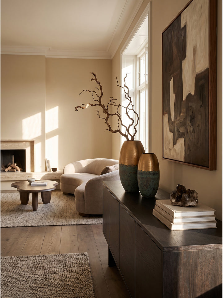 Das zweiteilige Set Aluminium-Dekovasen in Gold und patiniertem Türkis auf einem dunklen Eichen-Sideboard im stilvollen Wohnzimmer neben abstrakter Kunst._