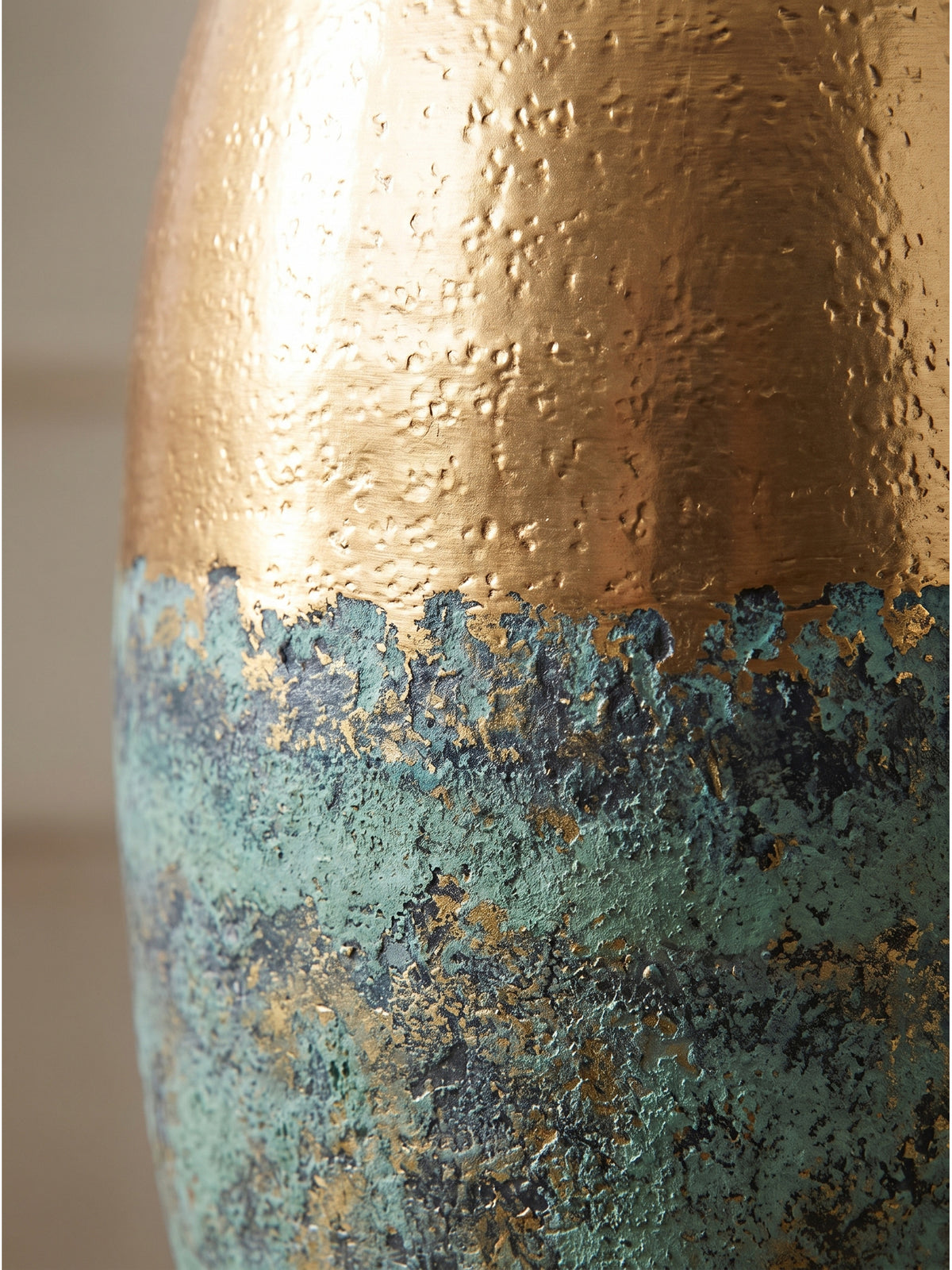 Nahaufnahme der handgefertigten Aluminium-Oberfläche mit feiner Hammerschlag-Punzierung im goldenen Bereich und rauer Vintage-Patina im türkisgrünen unteren Teil.