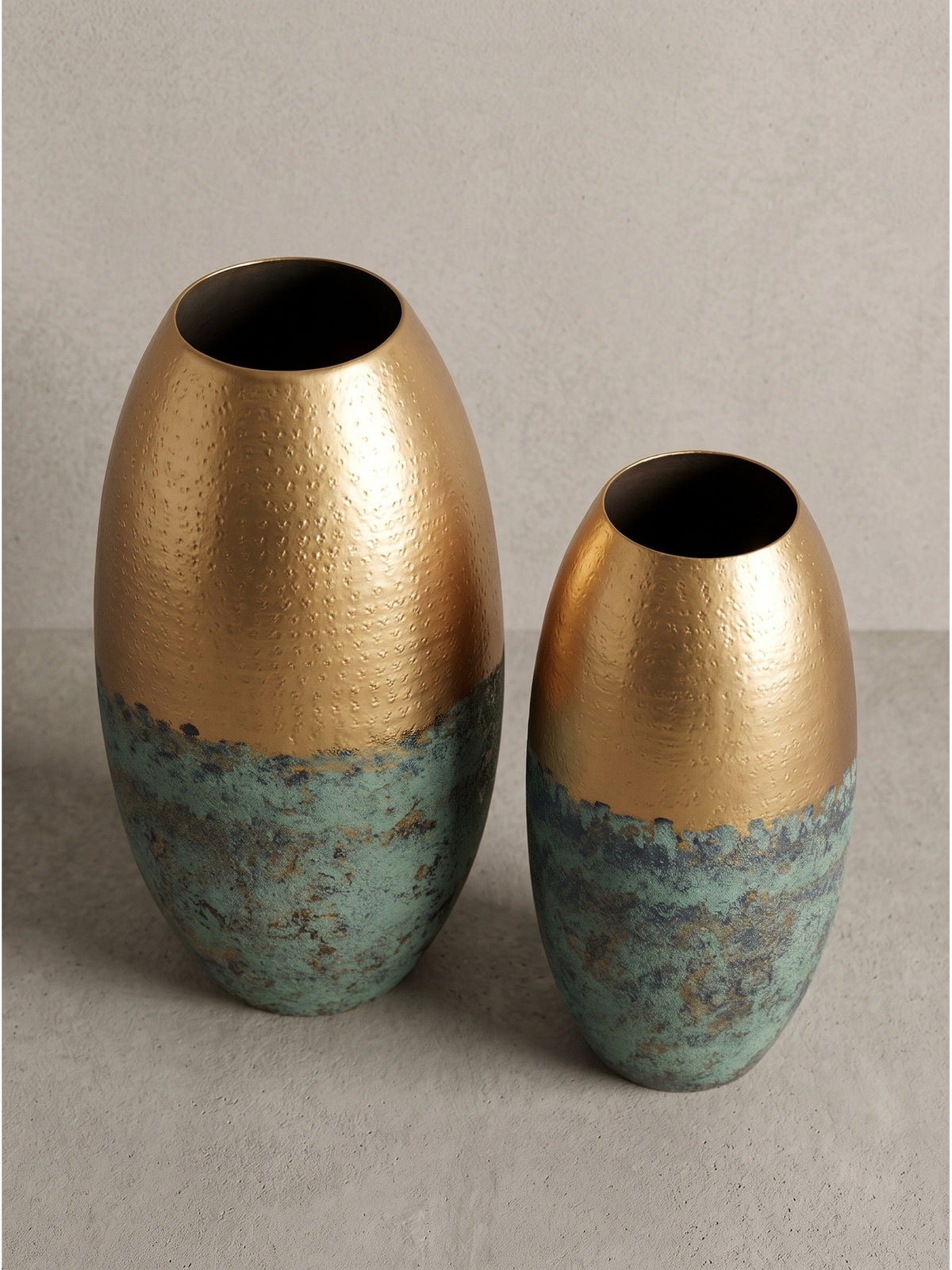 Ovale Blumenvase im modernen Zweifarben-Design aus gold lackiertem Aluminium und grob strukturierter Patina in leicht angewinkelter Perspektive aufgenommen._