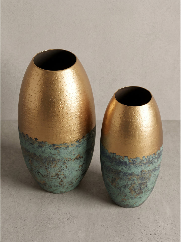 Ovale Blumenvase im modernen Zweifarben-Design aus gold lackiertem Aluminium und grob strukturierter Patina in leicht angewinkelter Perspektive aufgenommen._