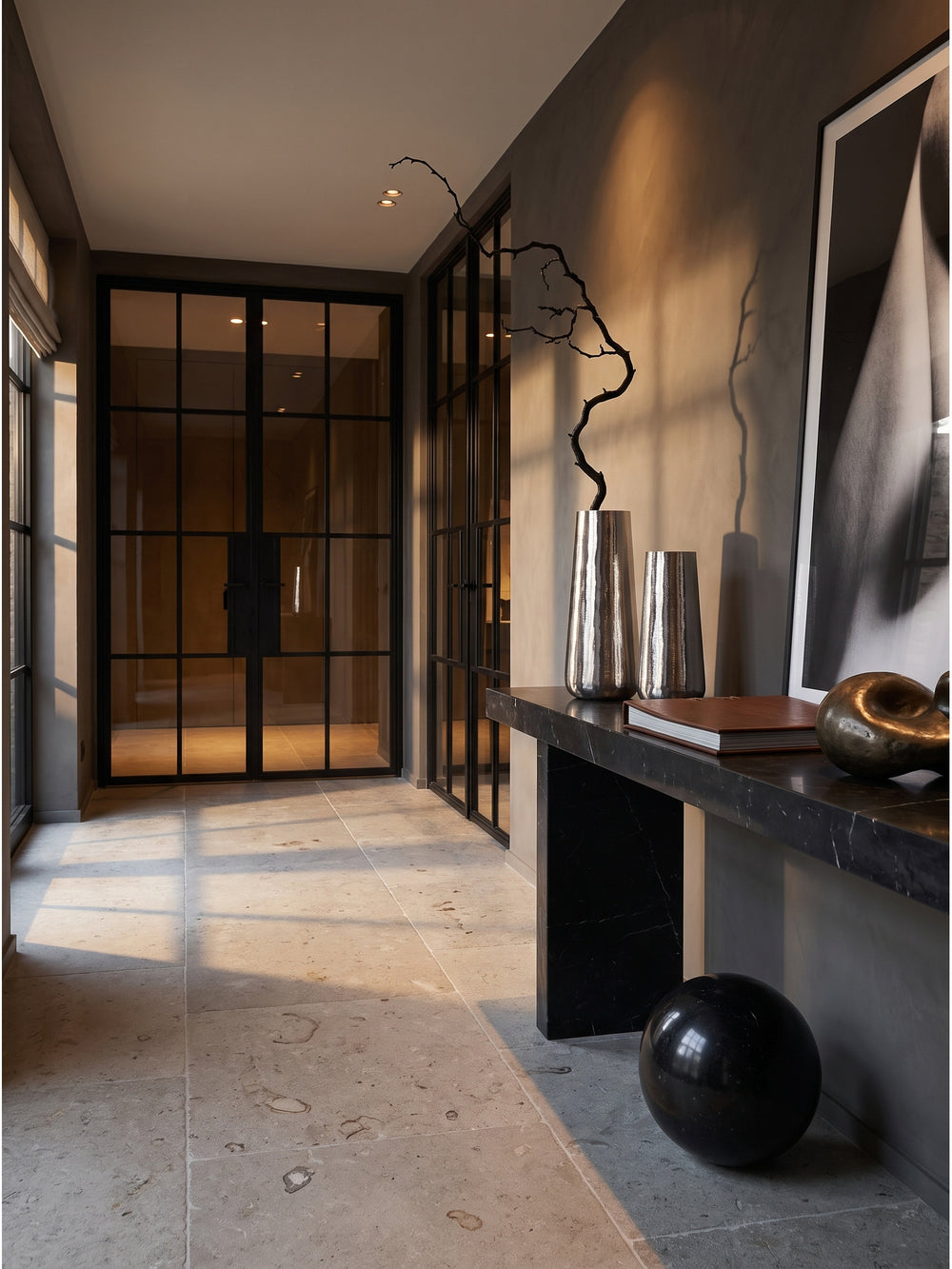 Elegantes Set aus zwei silbernen Aluminium-Vasen auf einer schwarzen Marmorkonsole im minimalistischen Flur mit anthrazitfarbener Tadelakt-Wand._