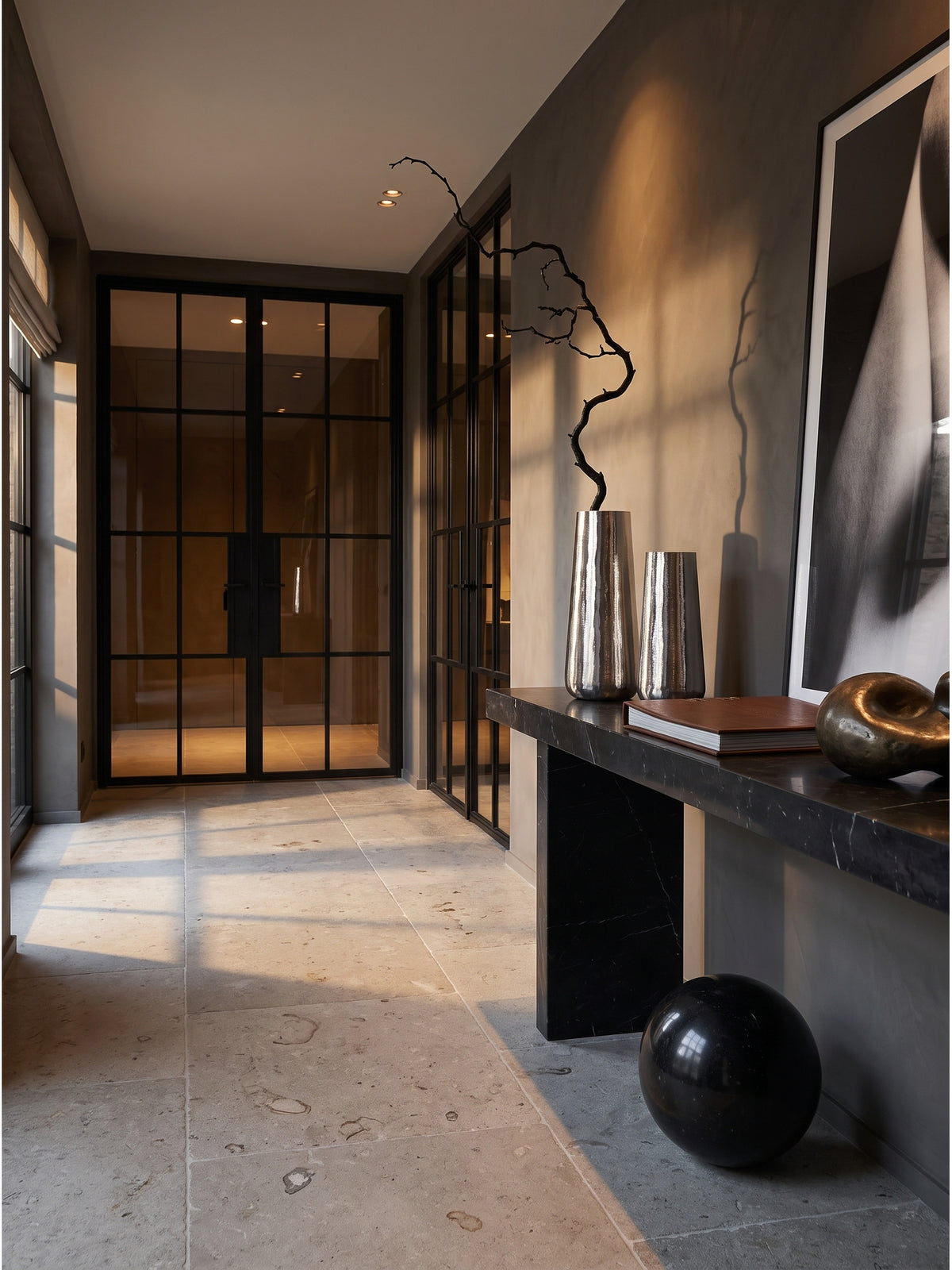 Elegantes Set aus zwei silbernen Aluminium-Vasen auf einer schwarzen Marmorkonsole im minimalistischen Flur mit anthrazitfarbener Tadelakt-Wand.